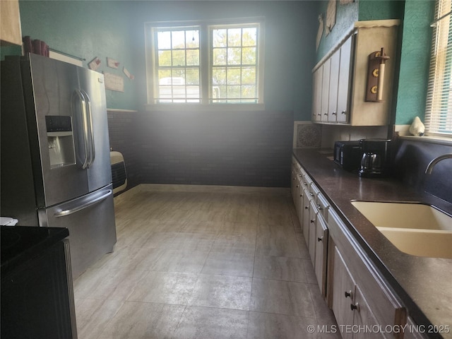 kitchen featuring dark countertops, baseboards, a sink, and stainless steel fridge with ice dispenser