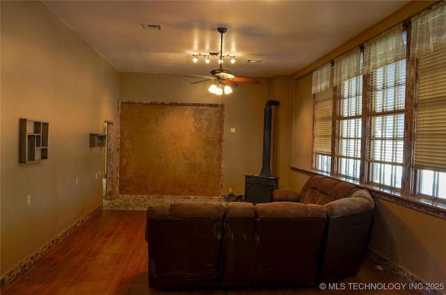 living area featuring wood finished floors, ceiling fan, a wood stove, baseboards, and visible vents