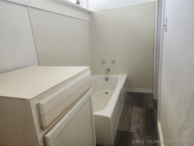 bathroom featuring a bath, baseboards, and wood finished floors