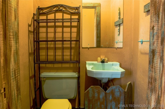 half bath featuring toilet, a textured wall, and a sink