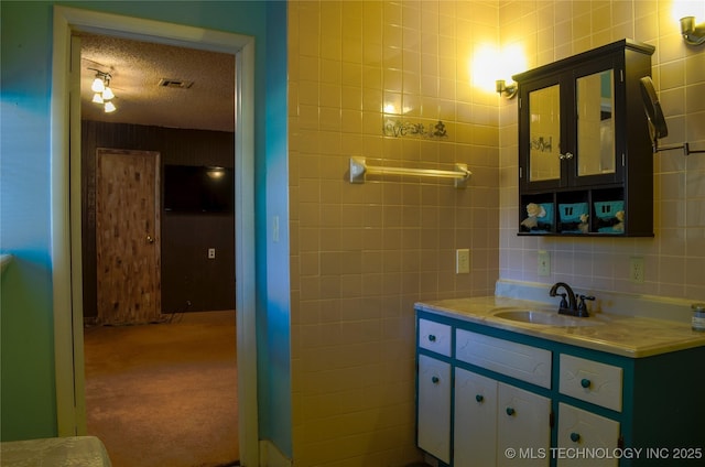 bathroom featuring a textured ceiling, tasteful backsplash, tile walls, visible vents, and vanity