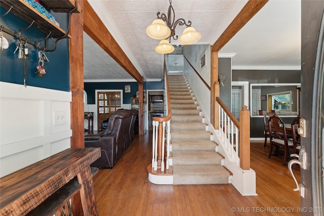 stairway with a chandelier, wood finished floors, crown molding, and wainscoting