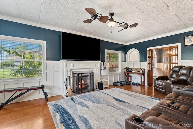 living room with a ceiling fan, wood finished floors, a wainscoted wall, and crown molding