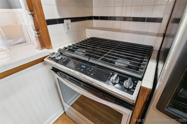 room details with backsplash, refrigerator, tile countertops, and gas range