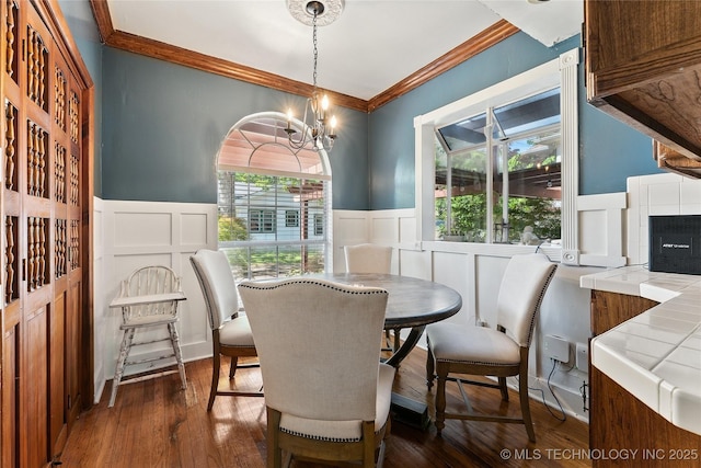 dining area featuring dark wood-type flooring, a decorative wall, ornamental molding, and wainscoting