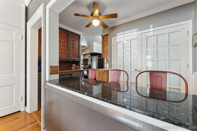 kitchen with wood finished floors, ornamental molding, dark stone counters, stainless steel refrigerator with ice dispenser, and ceiling fan