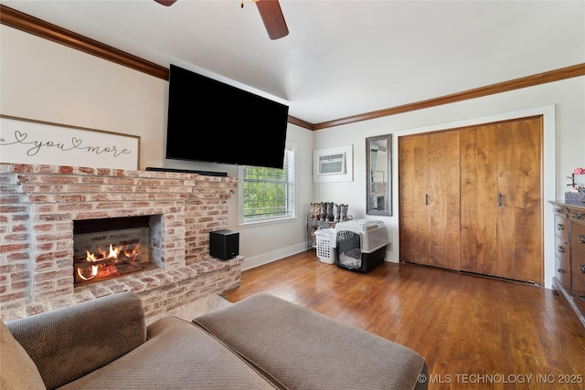 living room featuring wood finished floors, a ceiling fan, crown molding, baseboards, and a brick fireplace