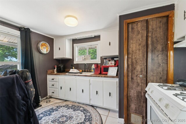 kitchen featuring white cabinets, dark countertops, white range with gas stovetop, a sink, and light tile patterned flooring