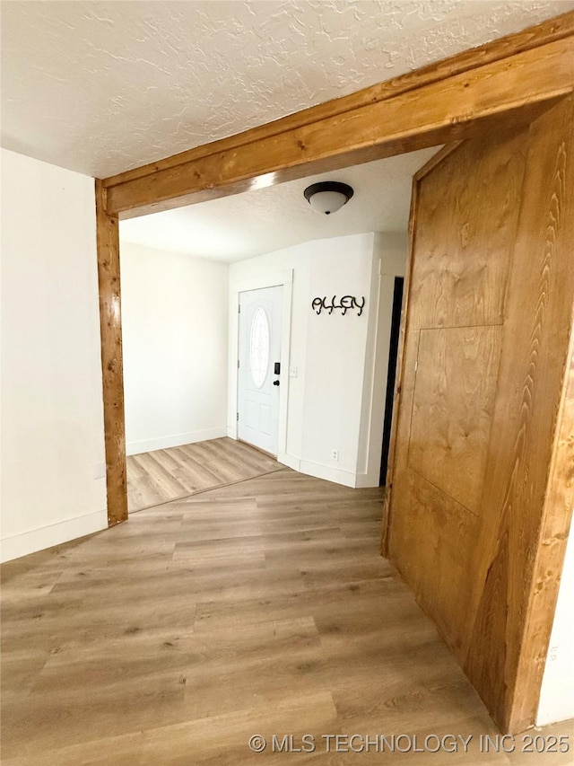 interior space with baseboards, beam ceiling, wood finished floors, and a textured ceiling
