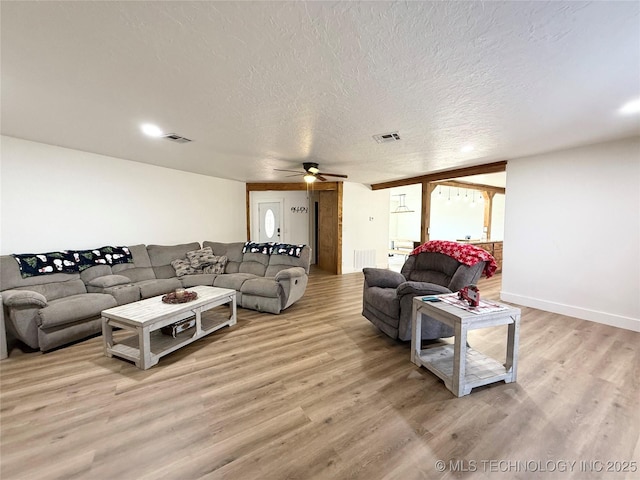 living room with light wood-style floors, visible vents, a ceiling fan, and a textured ceiling