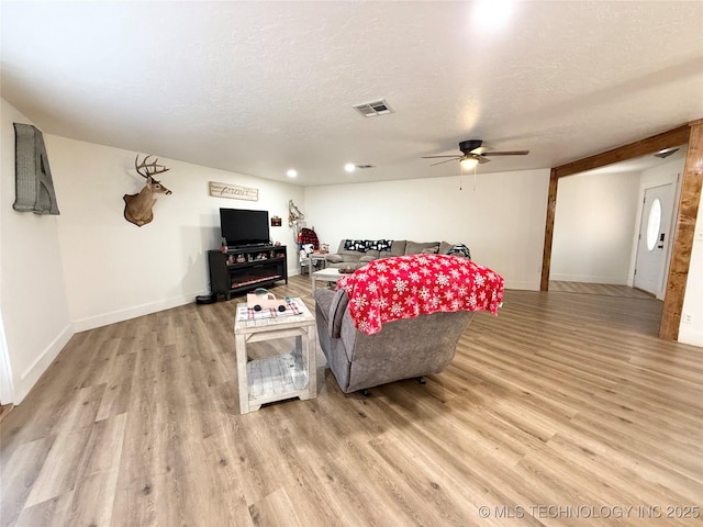 living area featuring a textured ceiling, light wood-type flooring, visible vents, and ceiling fan
