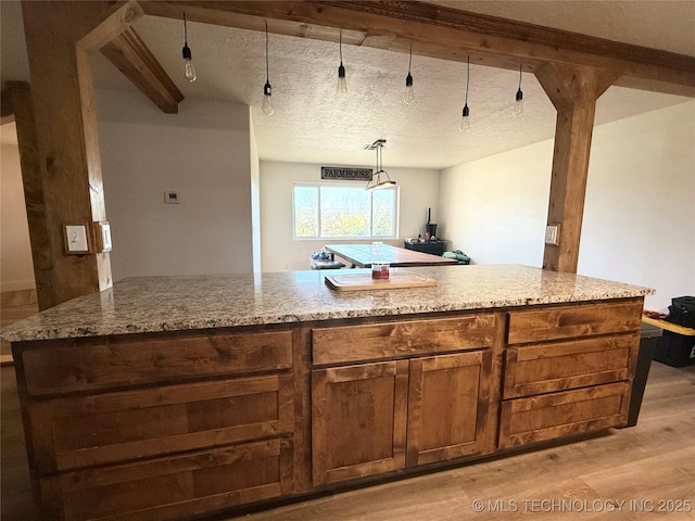 kitchen with beamed ceiling, light wood-style flooring, and light stone counters