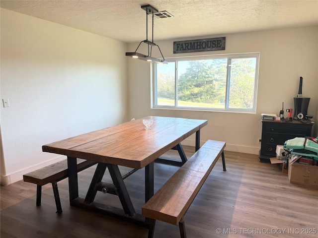 dining space with baseboards, wood finished floors, a textured ceiling, and visible vents