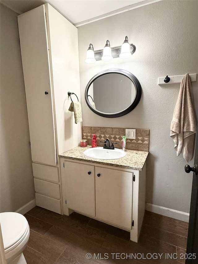 half bath featuring baseboards, toilet, vanity, and wood finished floors