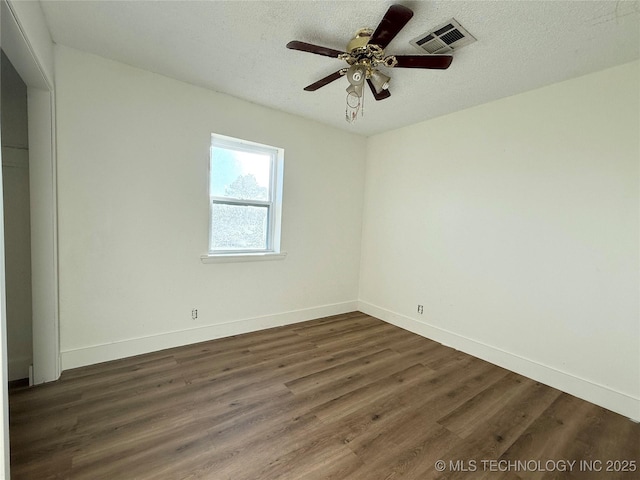 empty room featuring a ceiling fan, a textured ceiling, dark wood finished floors, baseboards, and visible vents