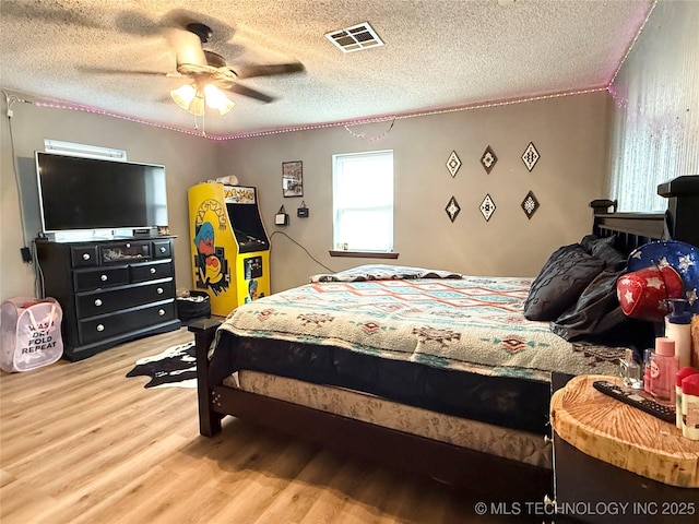 bedroom with ceiling fan, wood finished floors, visible vents, and a textured ceiling