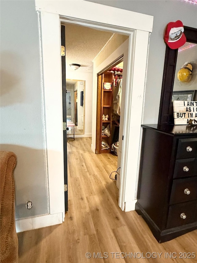 hall featuring baseboards, a textured ceiling, and light wood finished floors