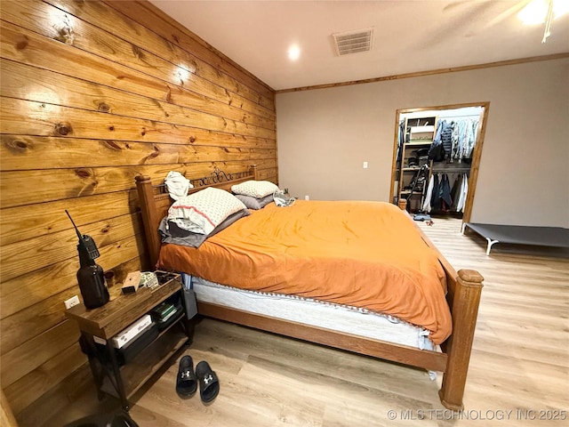 bedroom with a walk in closet, crown molding, wood finished floors, and visible vents