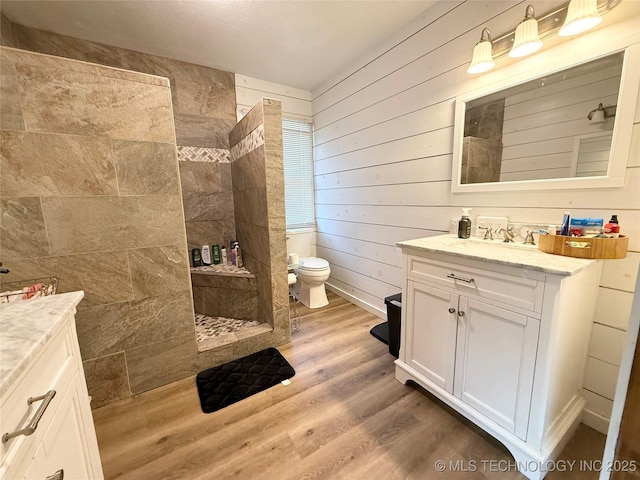 bathroom with wood finished floors, vanity, wooden walls, walk in shower, and toilet