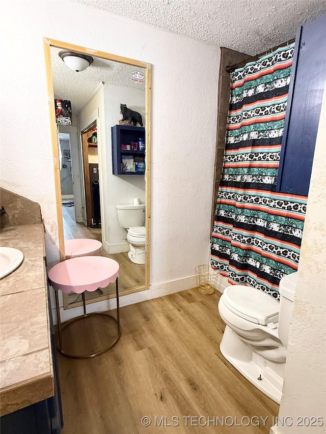 bathroom with vanity, toilet, wood finished floors, and a textured ceiling