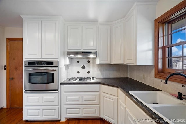 509 NE 10th St, Wagoner, OK 74467 - kitchen featuring a sink, appliances with stainless steel finishes, white cabinetry, backsplash, and under cabinet range hood