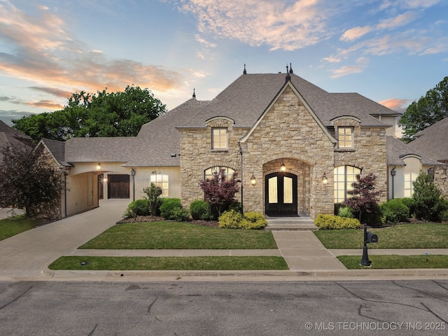 10626 S Joplin Ave, Tulsa, OK 74137 - french country home featuring french doors, stone siding, a front lawn, and roof with shingles