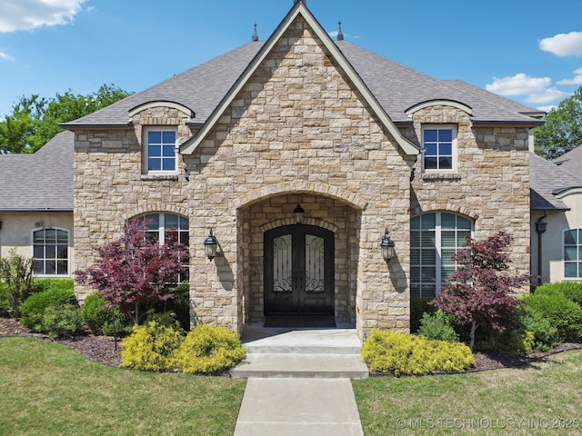 10626 S Joplin Ave, Tulsa, OK 74137 - french country inspired facade with a shingled roof, stone siding, a front yard, and french doors