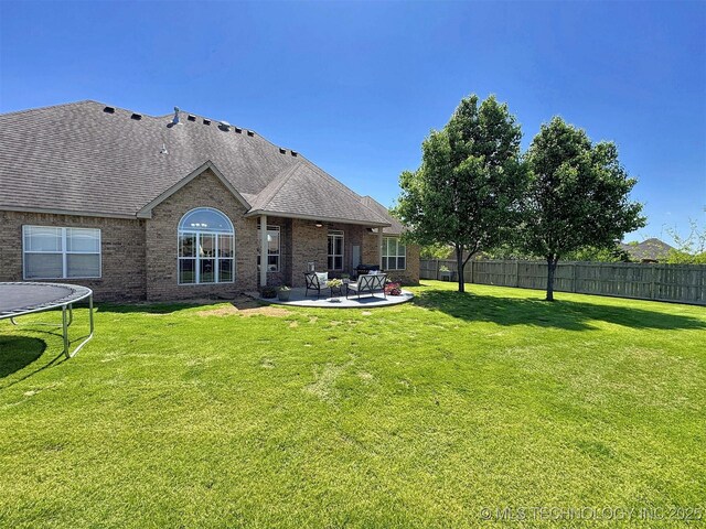 1412 Richmond Dr, Fort Gibson, OK 74434 - back of property featuring a patio area, a trampoline, a lawn, fence, and roof with shingles