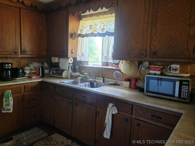kitchen with stainless steel microwave, light countertops, brown cabinets, and a sink