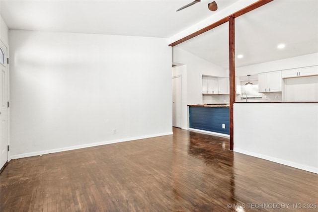 unfurnished living room featuring baseboards, wood finished floors, lofted ceiling with beams, and ceiling fan