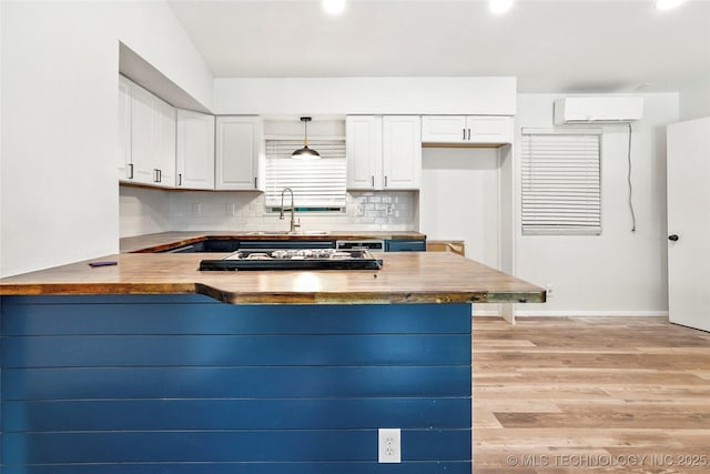 kitchen featuring a peninsula, a sink, light wood-style floors, white cabinetry, and a wall mounted AC