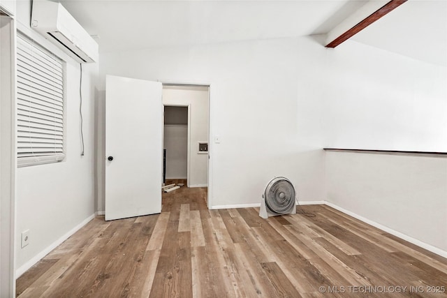 interior space featuring light wood finished floors, vaulted ceiling with beams, baseboards, and a wall mounted AC