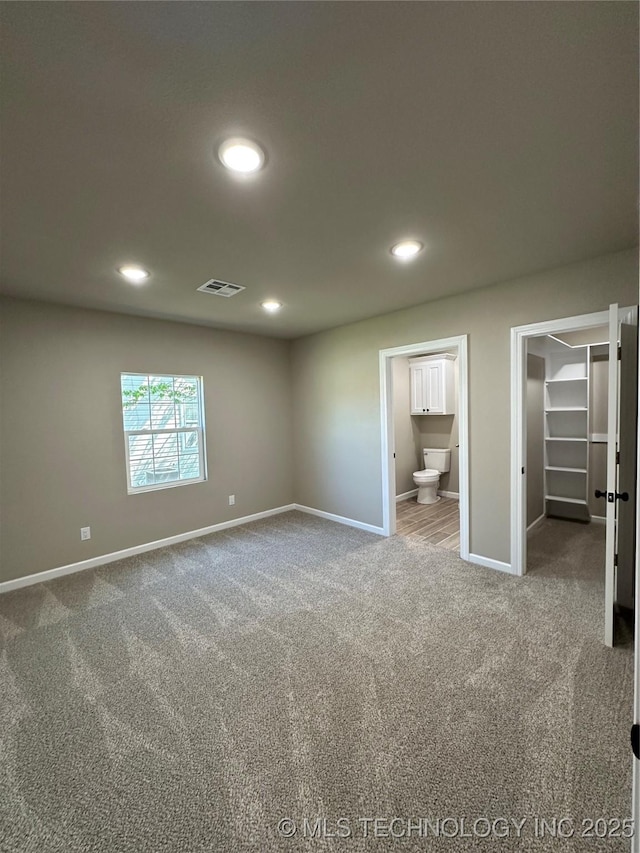 unfurnished bedroom featuring a walk in closet, baseboards, carpet flooring, visible vents, and recessed lighting