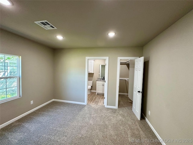 unfurnished bedroom with baseboards, visible vents, a spacious closet, light colored carpet, and connected bathroom