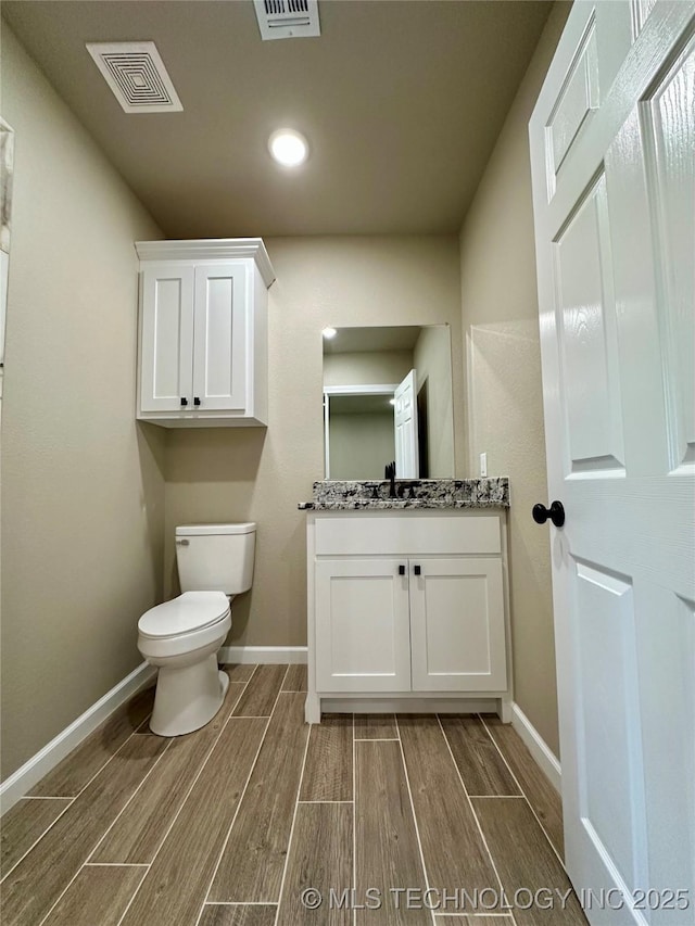 bathroom with wood finish floors, visible vents, toilet, and baseboards