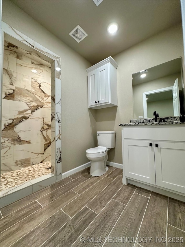 bathroom with a tile shower, toilet, visible vents, baseboards, and wood tiled floor