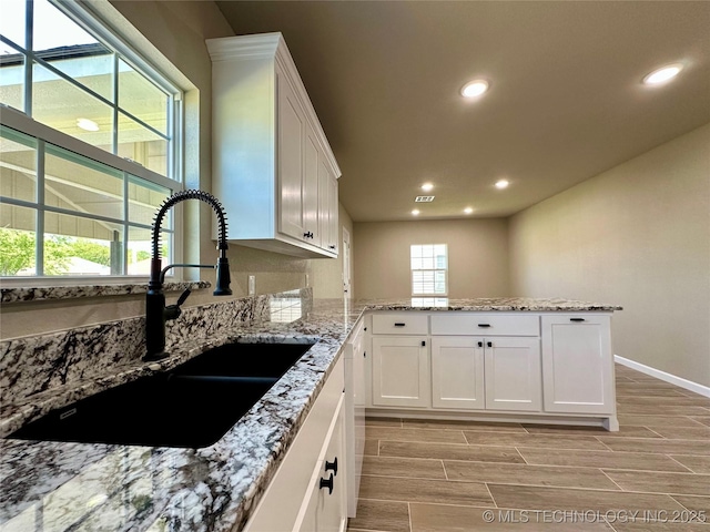 kitchen featuring recessed lighting, wood tiled floor, white cabinets, a sink, and a peninsula