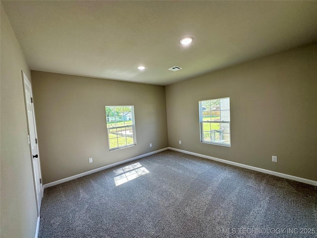 empty room featuring dark carpet, baseboards, and plenty of natural light