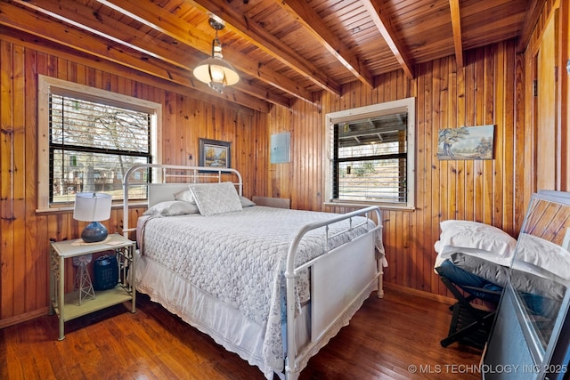 bedroom featuring beam ceiling, wood finished floors, multiple windows, and wooden walls