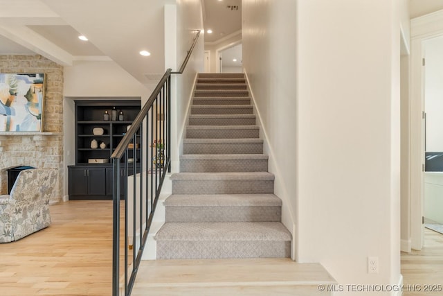 stairway featuring recessed lighting, wood finished floors, and a stone fireplace