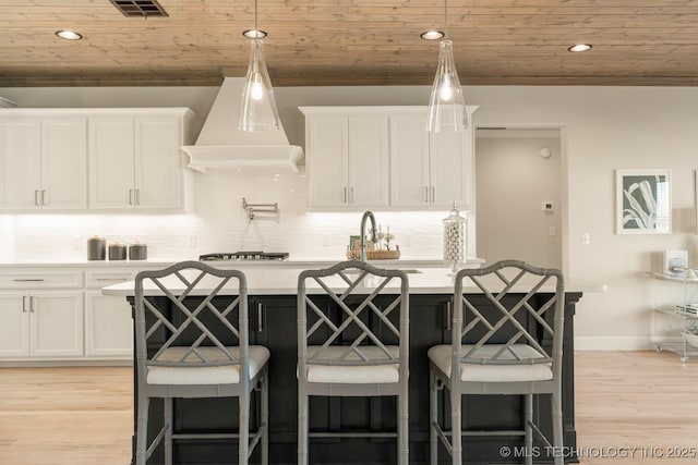 kitchen featuring custom exhaust hood, light countertops, white cabinets, and wood ceiling