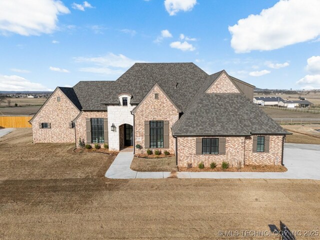french provincial home with brick siding, a front lawn, and roof with shingles