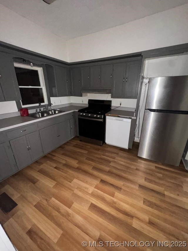 kitchen featuring a sink, light wood-type flooring, freestanding refrigerator, gray cabinetry, and gas stove