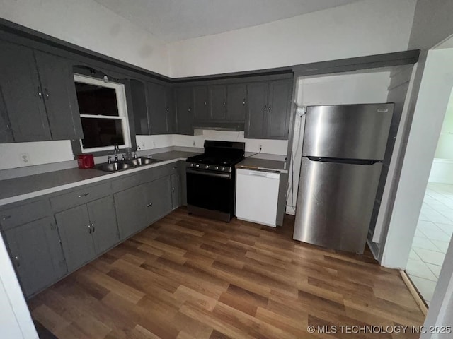 kitchen with a sink, exhaust hood, black gas range oven, dark wood-style flooring, and freestanding refrigerator