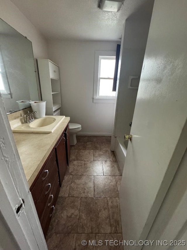 full bath with toilet, baseboards, stone finish floor, a shower, and vanity