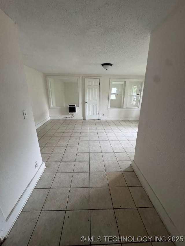 unfurnished living room with heating unit, baseboards, tile patterned flooring, and a textured ceiling