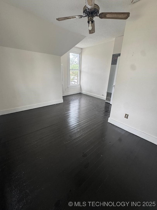 spare room with vaulted ceiling, a ceiling fan, a textured ceiling, baseboards, and dark wood-style floors