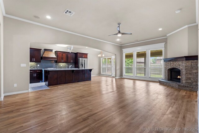 7056 E 124th St S, Bixby, OK 74008 - unfurnished living room featuring a chandelier, ornamental molding, ceiling fan, light wood-type flooring, and a stone fireplace