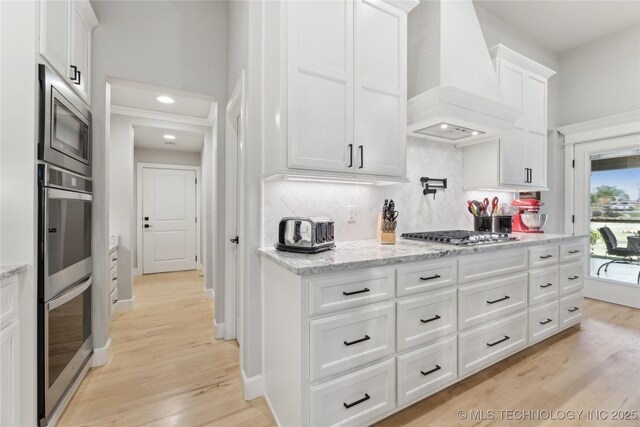 19340 E Canyon Ridge Rd, Owasso, OK 74055 - kitchen featuring stainless steel appliances, light wood-style flooring, backsplash, white cabinetry, and premium range hood