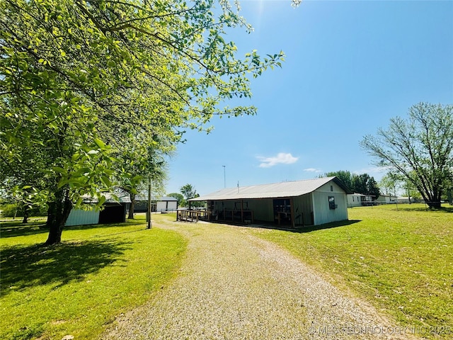 view of front of house featuring driveway, metal roof, a pole building, an outdoor structure, and a front yard